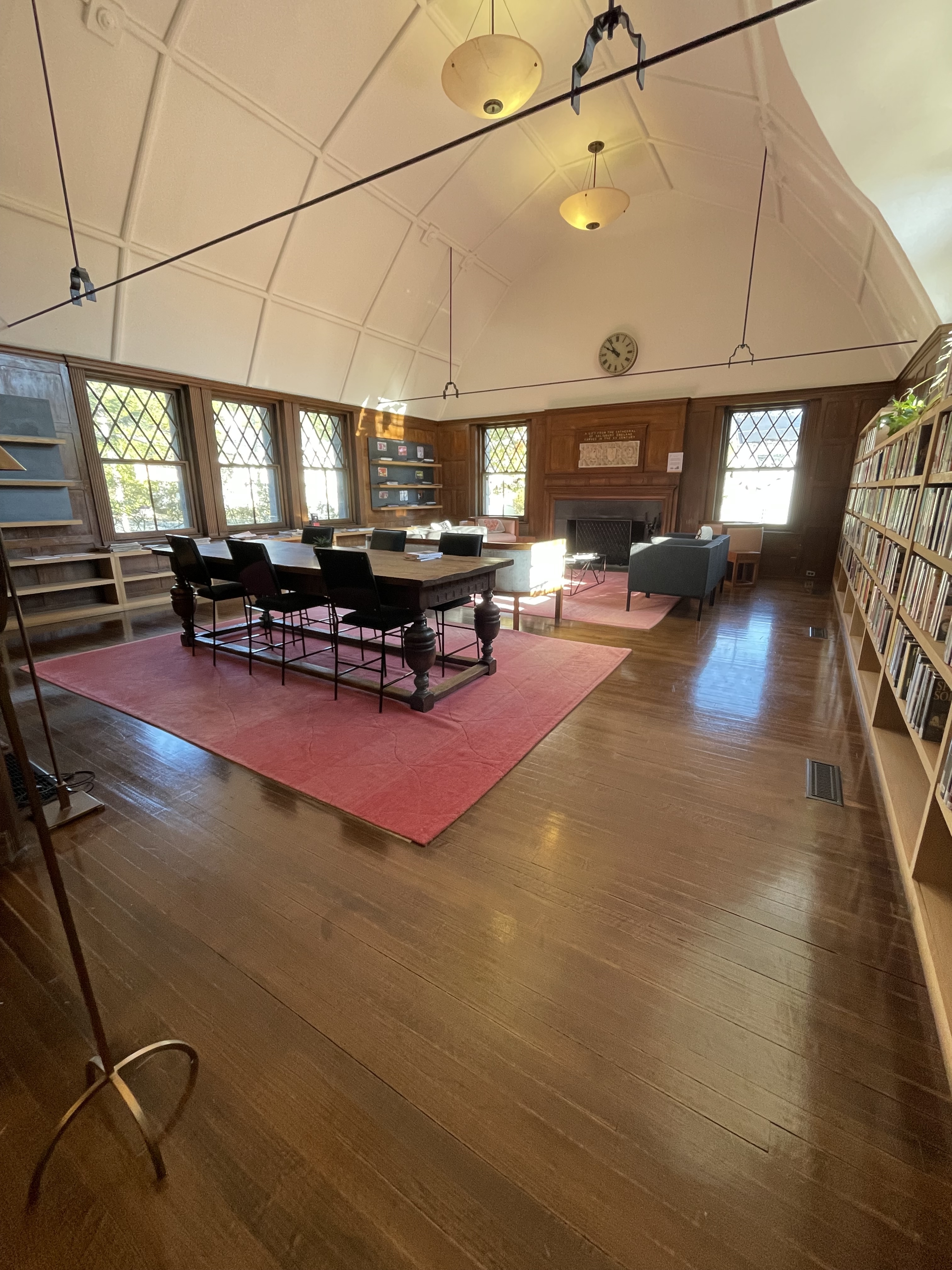 Large room with fire place, seating area, group table, book shelving and a barn-style ceiling