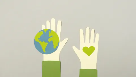 two hands, one holding a small globe, the other a small green heart